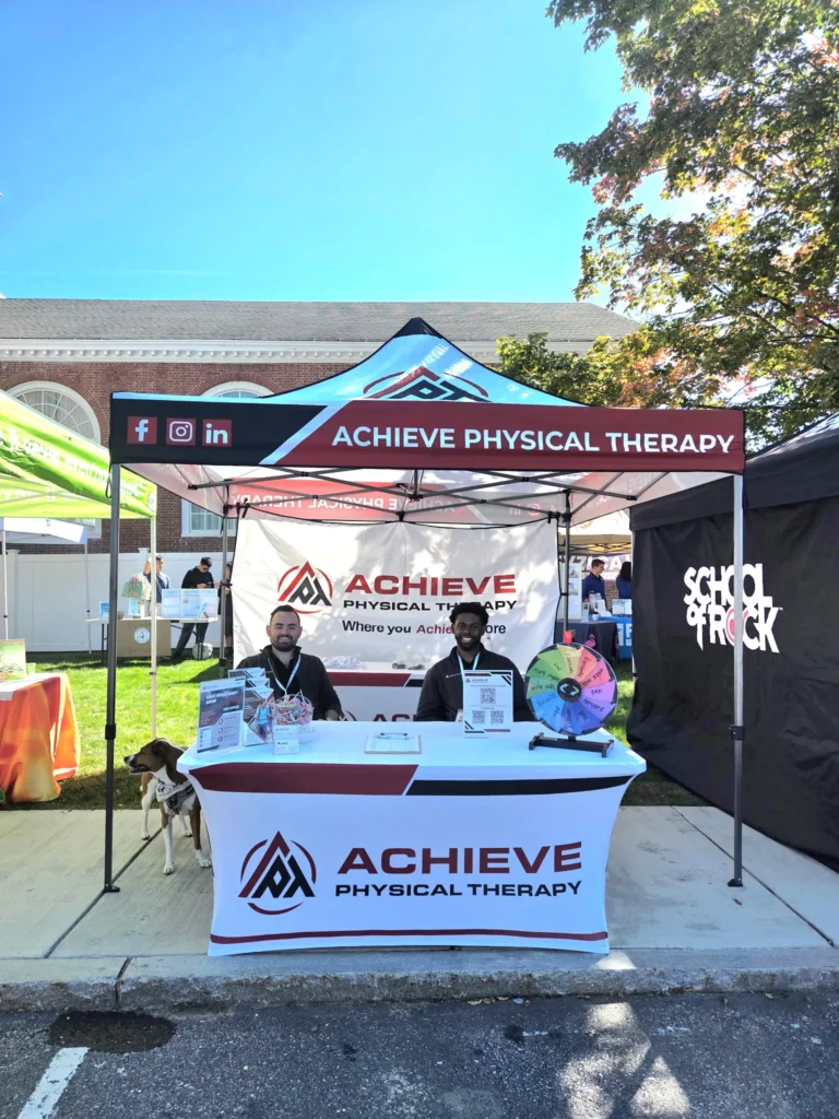 two employees site at Achieve Physical Therapy's tent during the Bedford Days community event, ready to answer questions